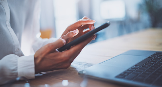 Photo of a women's hands with a cell phone and a laptop